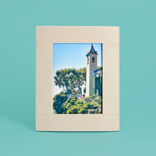 Load image into Gallery viewer, High-end leather picture frame with white contrast stitching. Holds 5x7" photo. Cream / white leather shown, standing vertically.