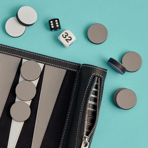 Close-up detail shot of luxury black leather travel backgammon set, showing leather backgammon board, white stitching, and leather pieces